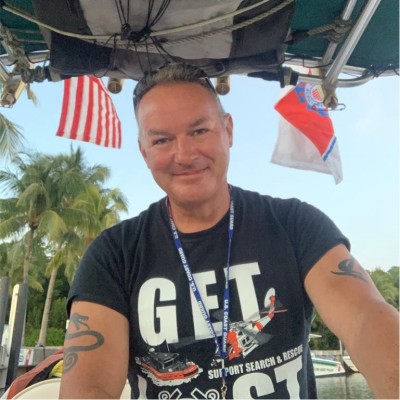 Photograph of Mark Chiappone smiling with two flags waving in the background.