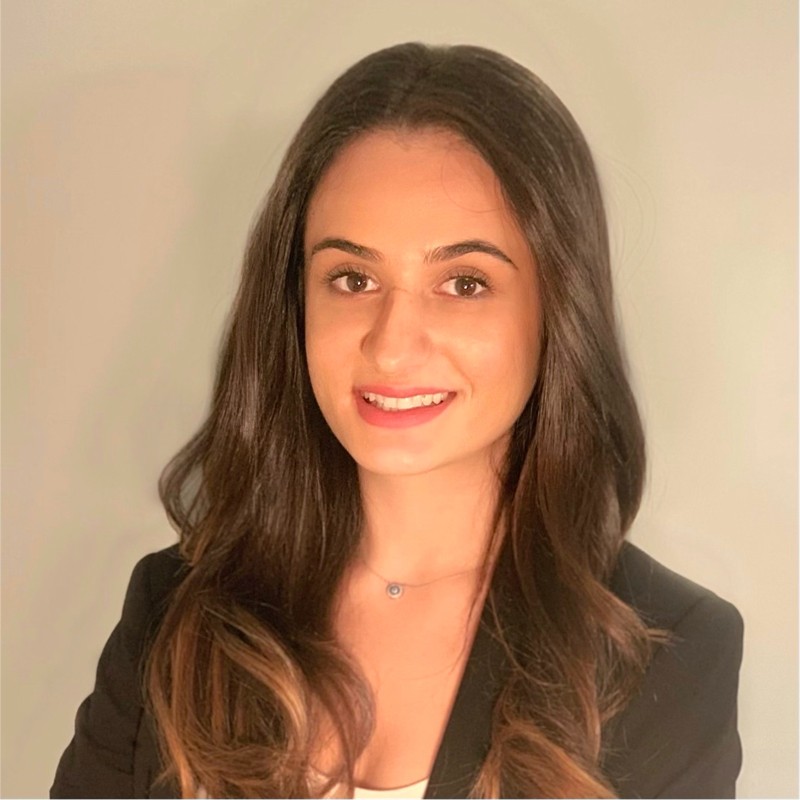 Nora Avdullahu standing in front of a beige background smiling for a photo.