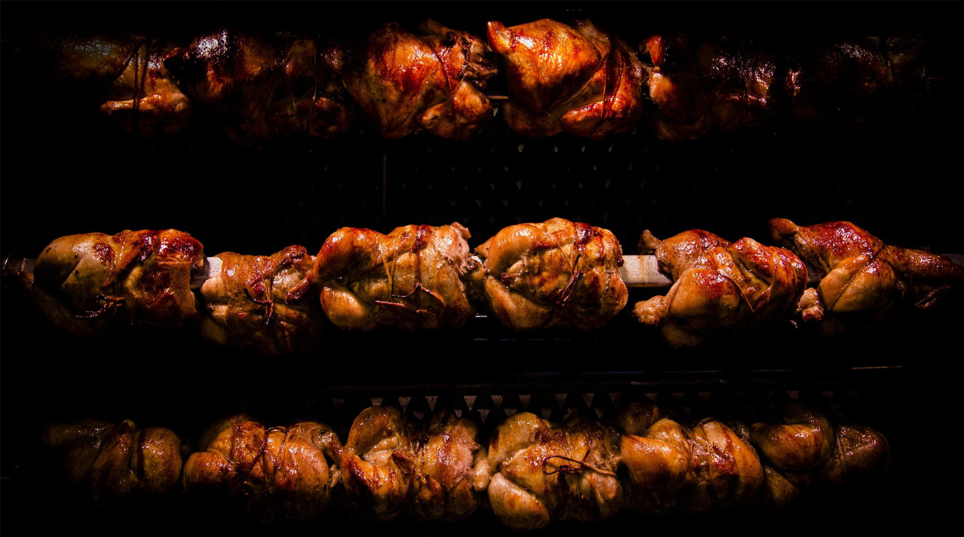Three Rows of Rotisseries Chicken lit up eerily in front of a pure black background.