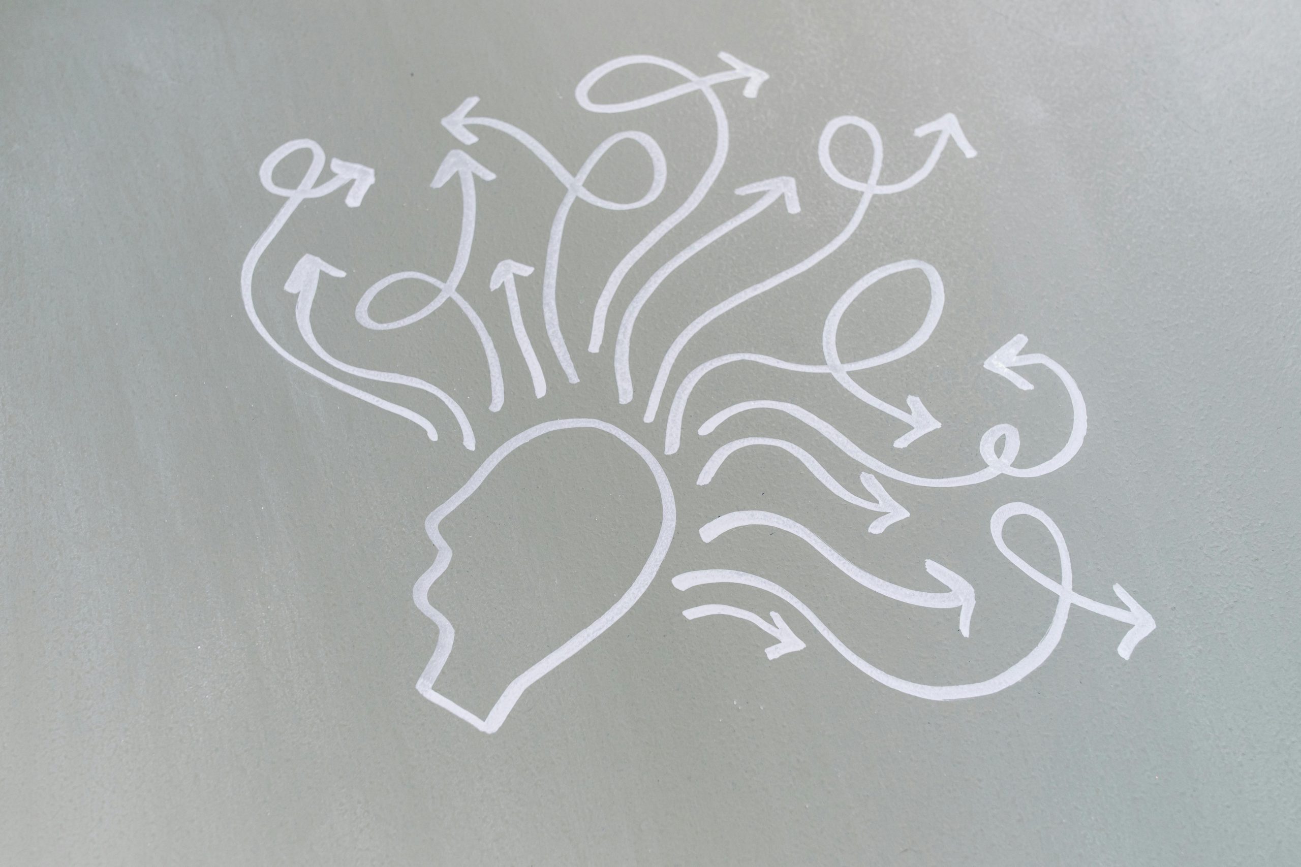 A gray canvas with a drawing of a head with squiggly arrows popping out of the line-art head drawing to represent the mind going in many places.